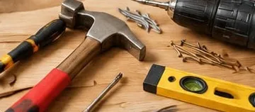Outils de bricolage sur un plan de travail en bois : marteau, perceuse, niveau et clous